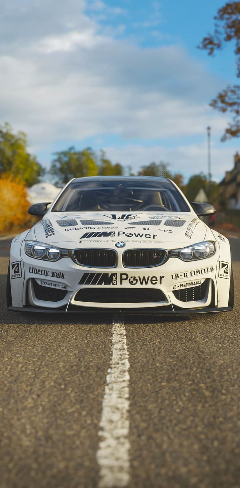 White BMW M4 with Liberty Walk widebody kit and M Power livery parked on an asphalt road under a cloudy sky.