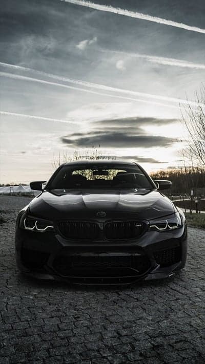 Black BMW M5 on Cobblestone Road Under Cloudy Sky