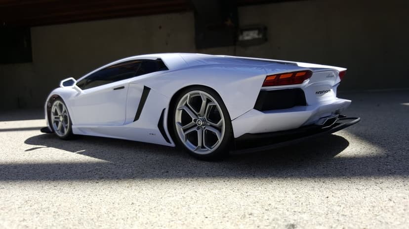 White Lamborghini Aventador rear end with Y-shaped taillights and sharp aerodynamic diffusers on a textured road.