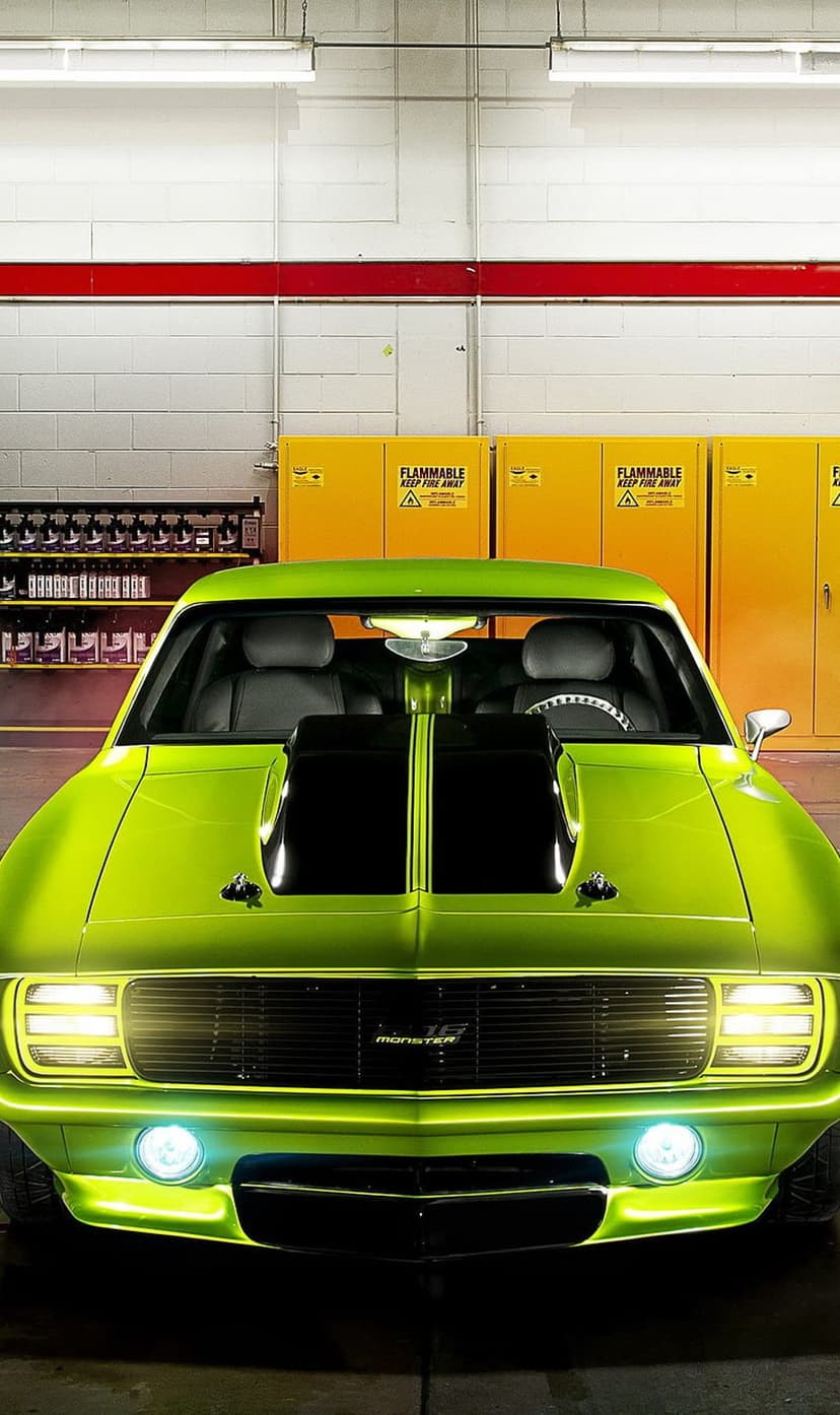 Lime green muscle car with black racing stripes parked inside a garage near yellow industrial storage cabinets.