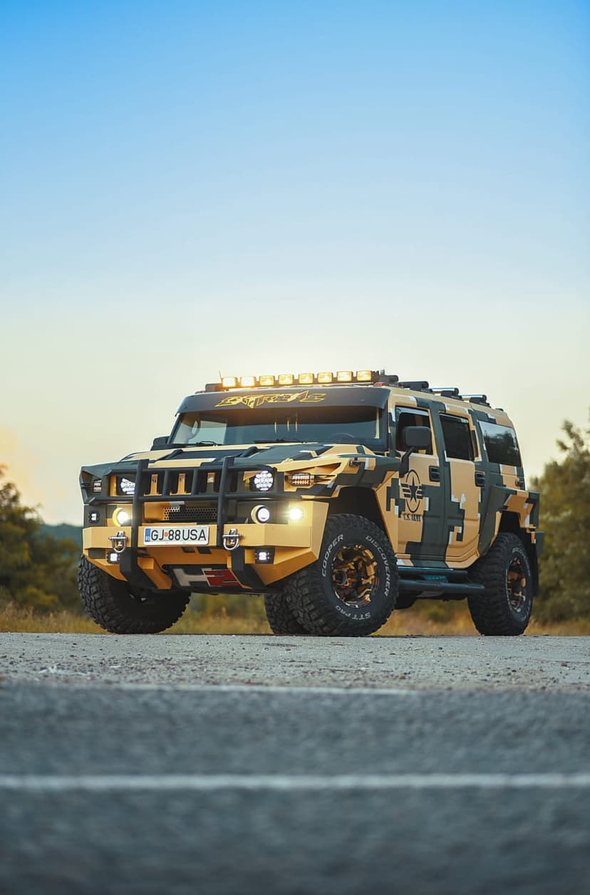 Hummer H2 with desert camouflage paint, roof-mounted LED lights, and off-road tires on a paved rural road.