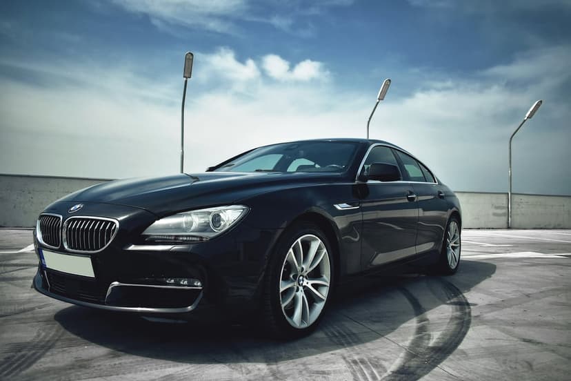 Black BMW 6 Series coupe parked on a concrete rooftop with tire marks under a cloudy sky and modern streetlights.