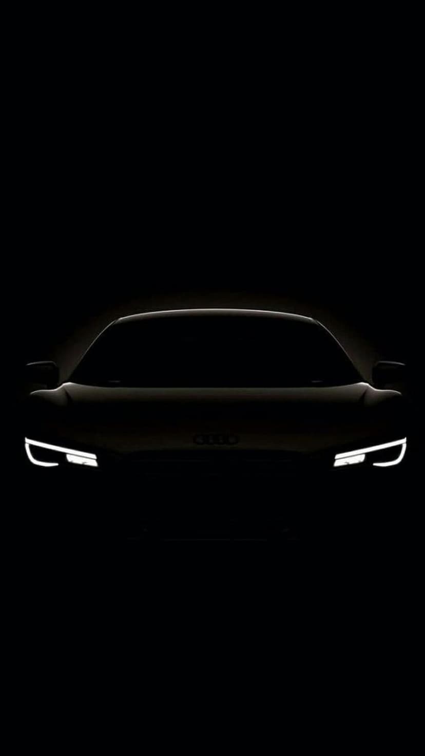 Audi R8 sports car silhouette with glowing LED headlights visible against a dark black night background.