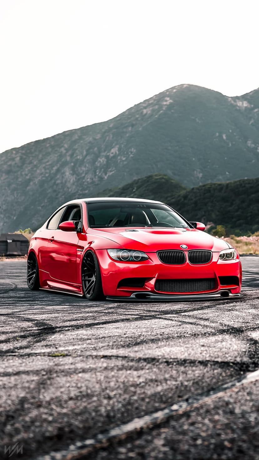 Red BMW M3 drifting on a rough asphalt road against a backdrop of hazy, jagged mountains under a clear sky.