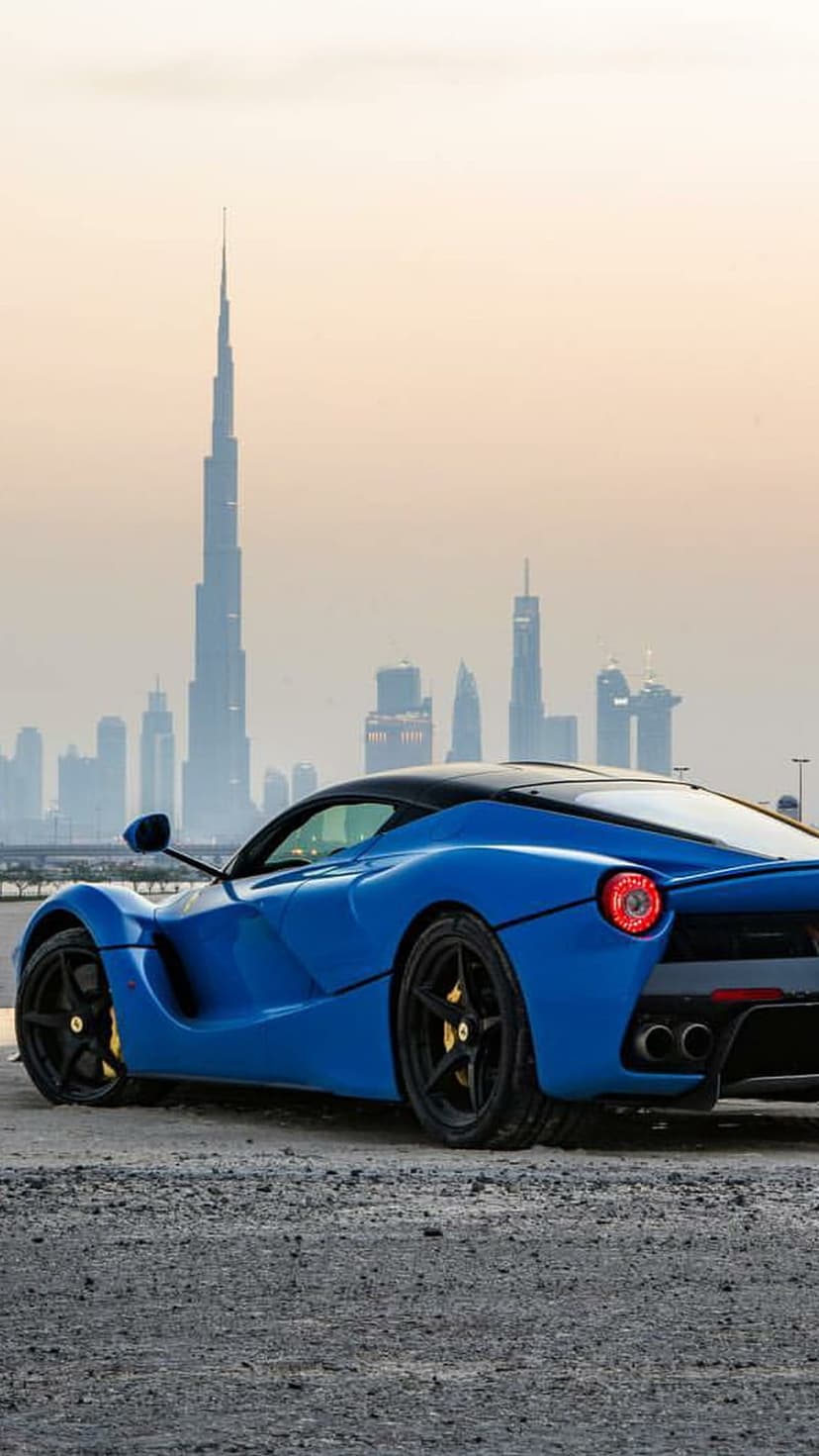 Blue Ferrari LaFerrari parked on a Dubai street with the Burj Khalifa and city skyscrapers in the background.
