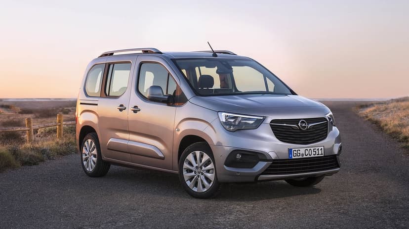 Silver Opel Combo Life passenger van parked on an asphalt path amidst grassy coastal dunes under a warm sunset sky.
