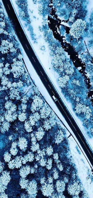 An elevated perspective captures a serene river winding through a vast forest ablaze with the golden and orange hues of autumn. Several small, tree-dotted islands are scattered along the river's path, adding visual interest. The sky above is a dramatic spectacle of warm, glowing clouds, bathed in the rich light of a sunset or sunrise, casting a soft, ethereal glow over the entire landscape.