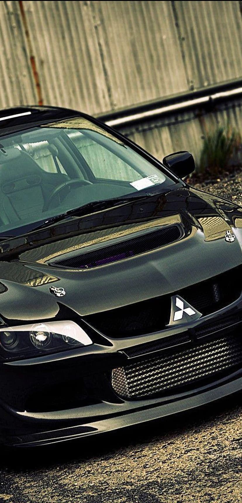 Mitsubishi Evolution car with a glossy black finish and carbon fiber hood features a low-angle front perspective.