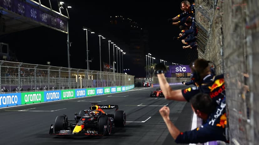A Red Bull Formula 1 car speeds past a celebrating pit crew under bright track lights during a night race finish.