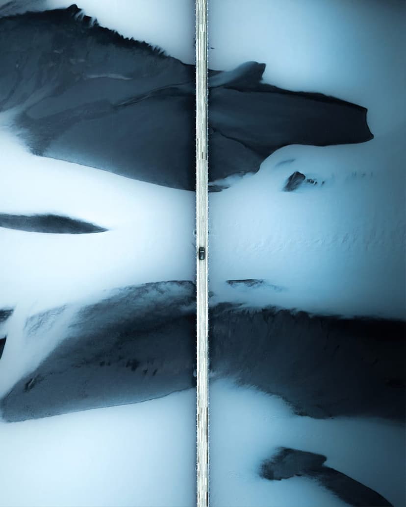 Small vehicle crossing a narrow bridge above intricate blue ice formations and frozen arctic water patterns.