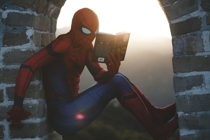 Spider-Man sits on the stone Great Wall of China reading a book during a golden sunset over mountain ridges.