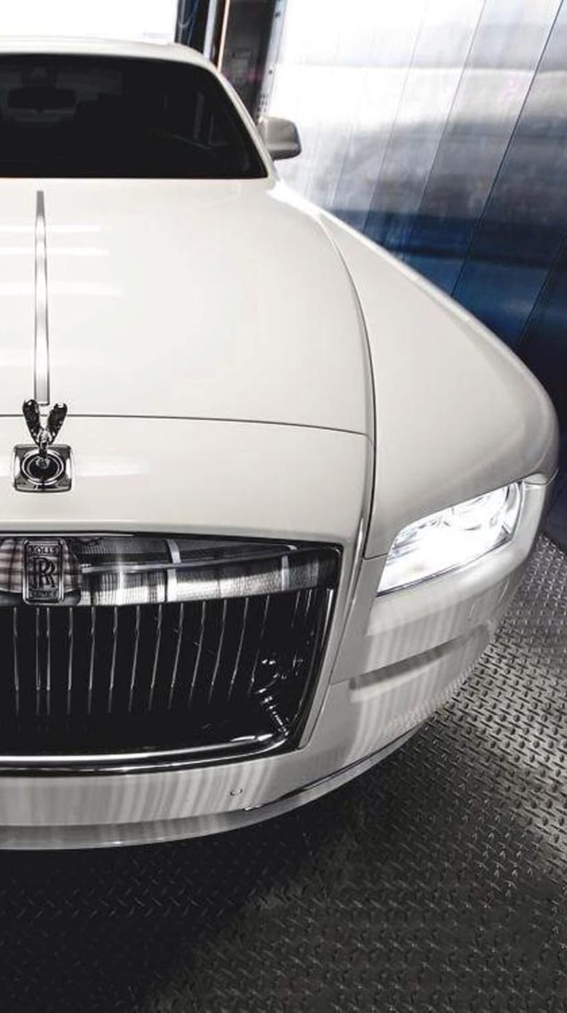 Rolls-Royce Ghost hood ornament and chrome grille with glowing headlights on a polished white luxury vehicle.