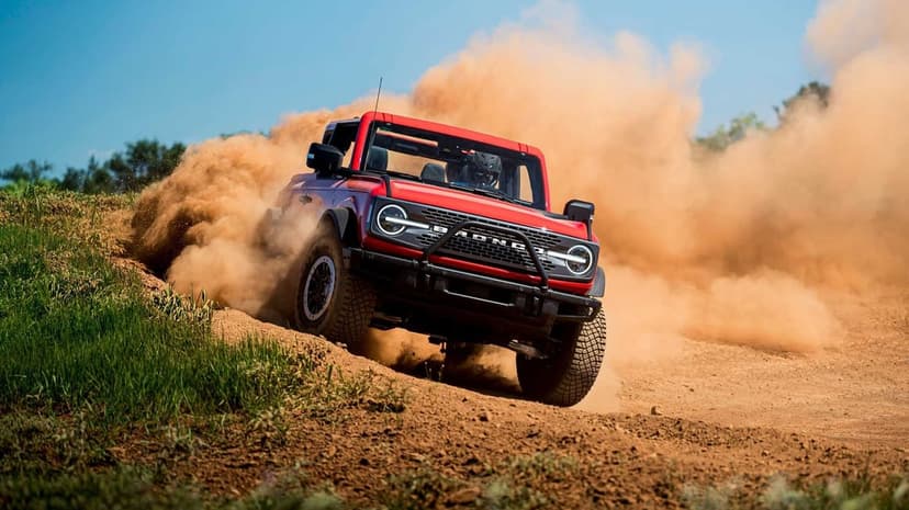 Red Ford Bronco SUV kicking up a massive cloud of brown dust while driving fast on a rugged dirt trail.