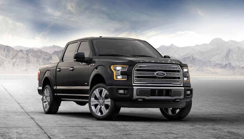 Black Ford F-150 Limited truck parked on a desert flat with mountains under a soft blue sky.