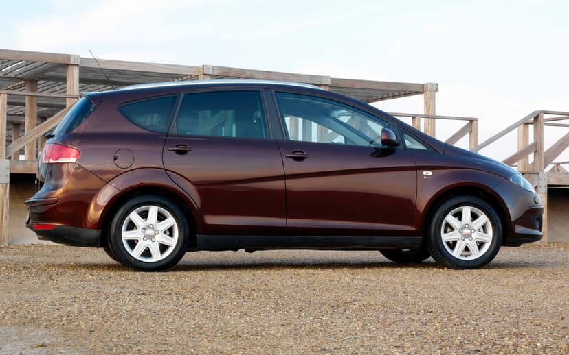 Dark maroon SEAT Altea car in side profile parked on gravel with a wooden beach structure background.