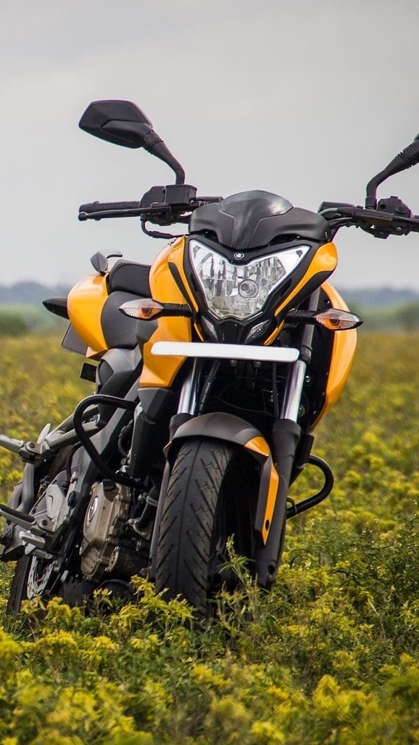 Yellow sportbike parked in a dense field of yellow wildflowers under a soft, overcast sky in a vertical view.
