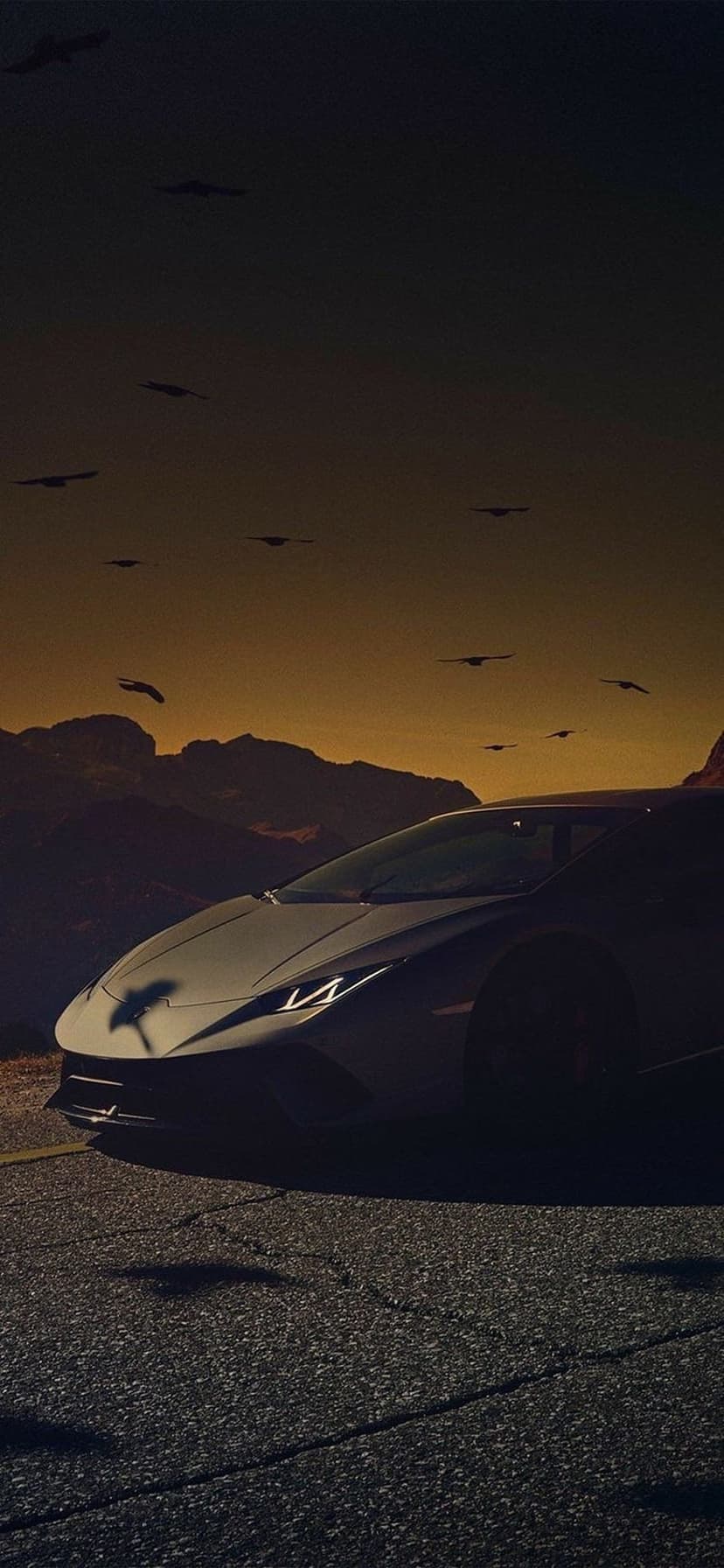 Dark luxury sports car with glowing headlights on a cracked road under a sunset sky with bird silhouettes.