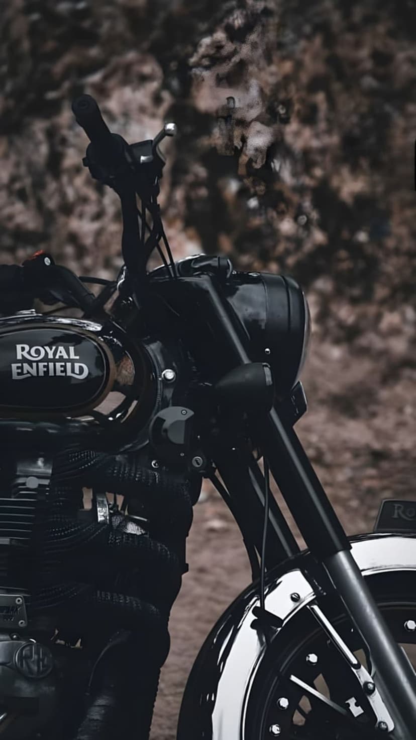 Royal Enfield motorcycle fuel tank with a silver logo, chrome handlebars, and a vintage round headlight.