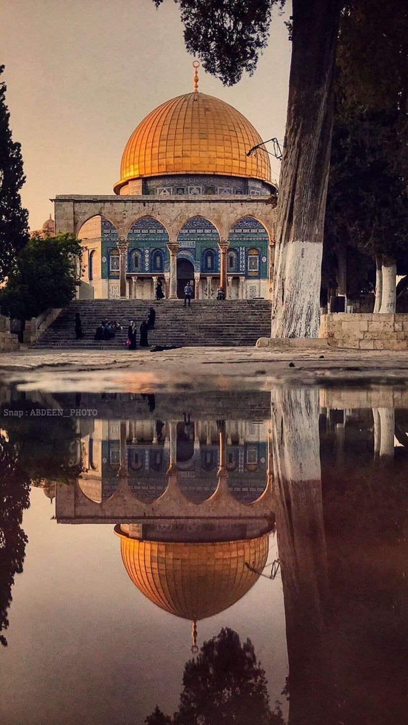 Dome of the Rock with its golden top reflected in a pool of water during a vibrant orange sunset in Jerusalem.