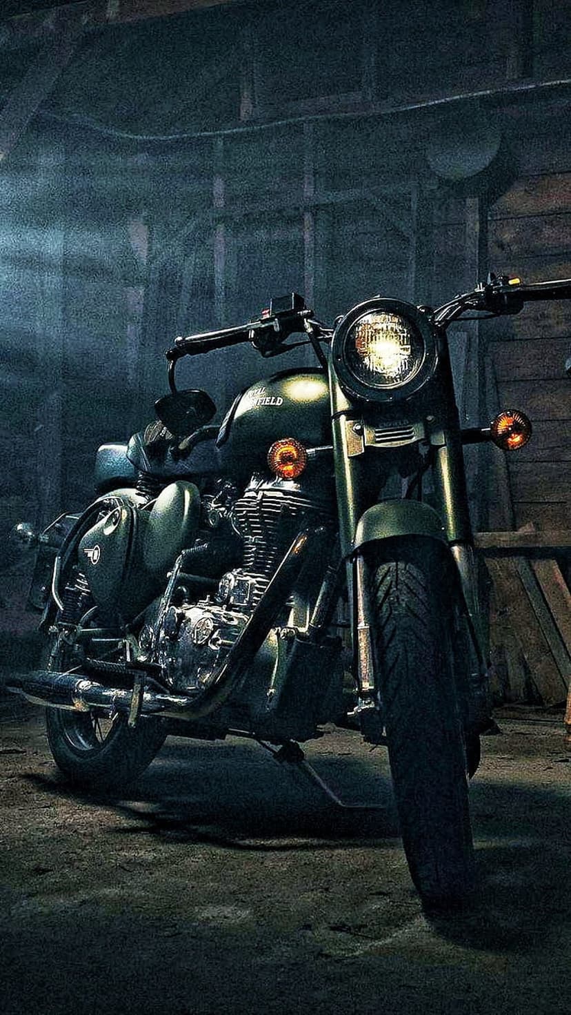 Olive green Royal Enfield motorcycle with chrome details parked in a dimly lit, rustic workshop garage.
