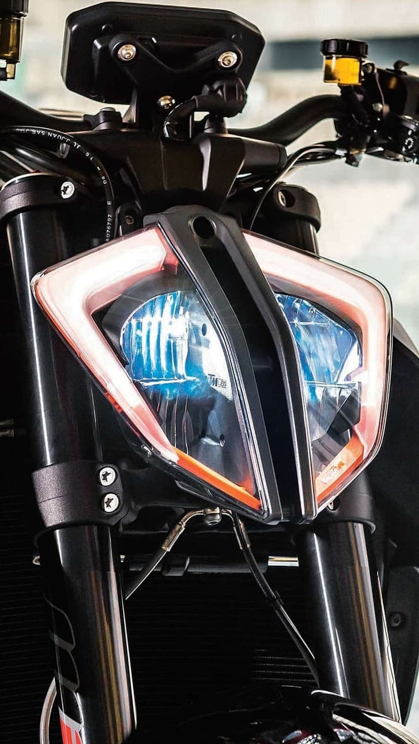 KTM motorcycle headlight assembly features sharp angular LEDs and a blue glowing bulb with visible fork tubes.