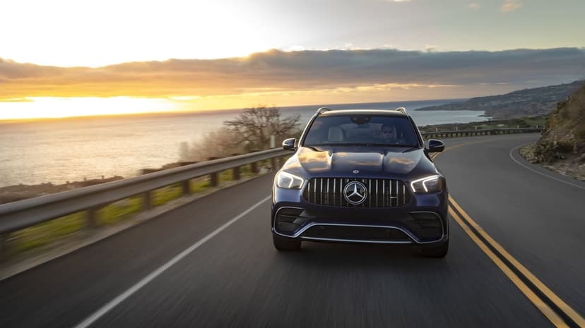 Mercedes-AMG SUV driving on a coastal winding road during a golden sunset with ocean waves in the background.