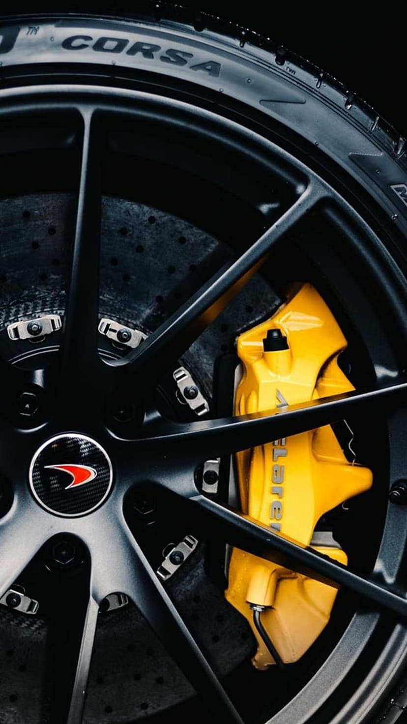 Matte black McLaren alloy wheel with bright yellow brake calipers and a carbon ceramic disc on a Pirelli tire.