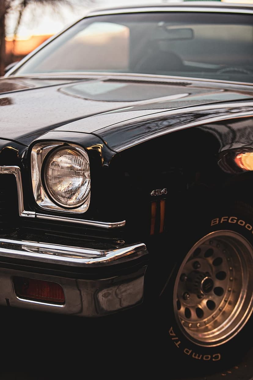 Classic black car front fender with chrome headlight bezel and a BFGoodrich tire reflecting a golden sunset.
