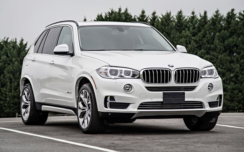 White BMW X5 luxury SUV in a low-angle front view on an asphalt lot with green trees in the background.