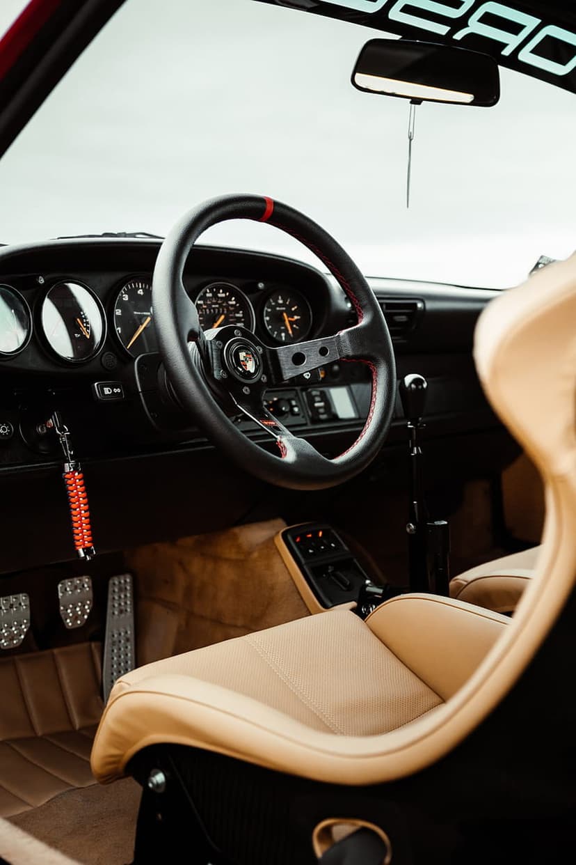 Porsche sports steering wheel with red stitching and tan leather racing seats inside a vintage car cabin.