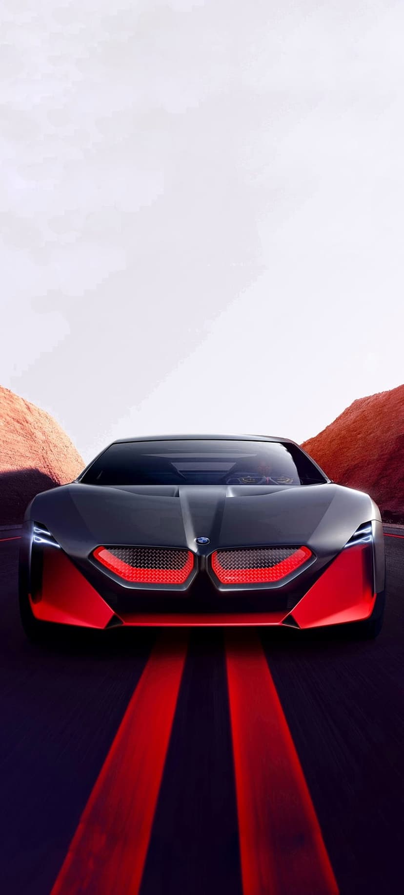 BMW concept car with glowing red grille lights driving on a dark road against a backdrop of rocky hills and sky.