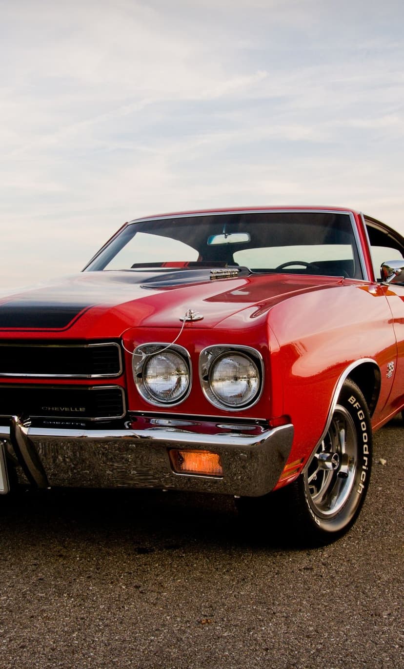 Front view of a red classic 1970 Chevelle SS with black hood stripes and chrome bumpers on a paved road.