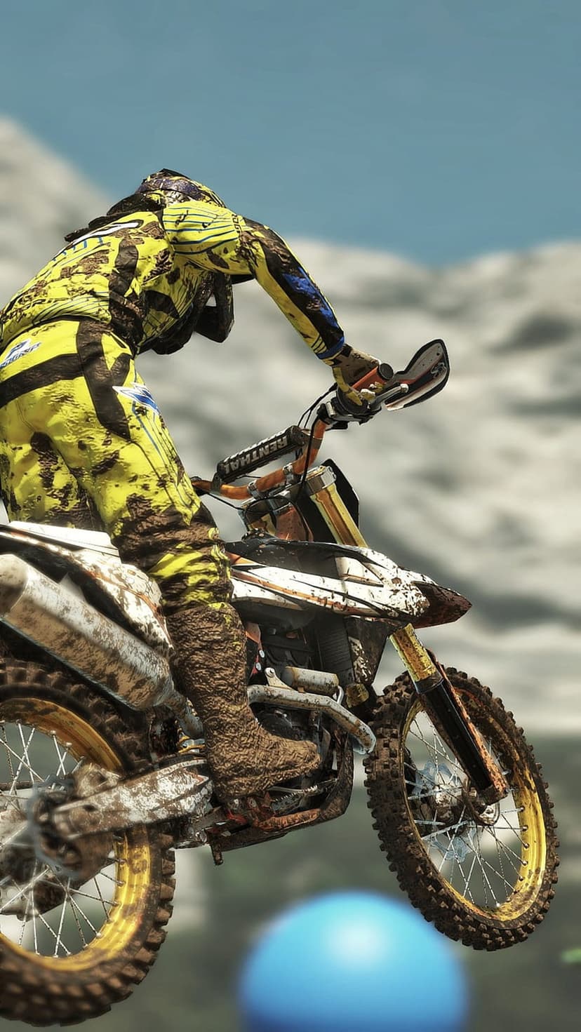 Motocross rider in mud-splattered yellow gear jumps a dirt bike with gold spokes against a clear sky.