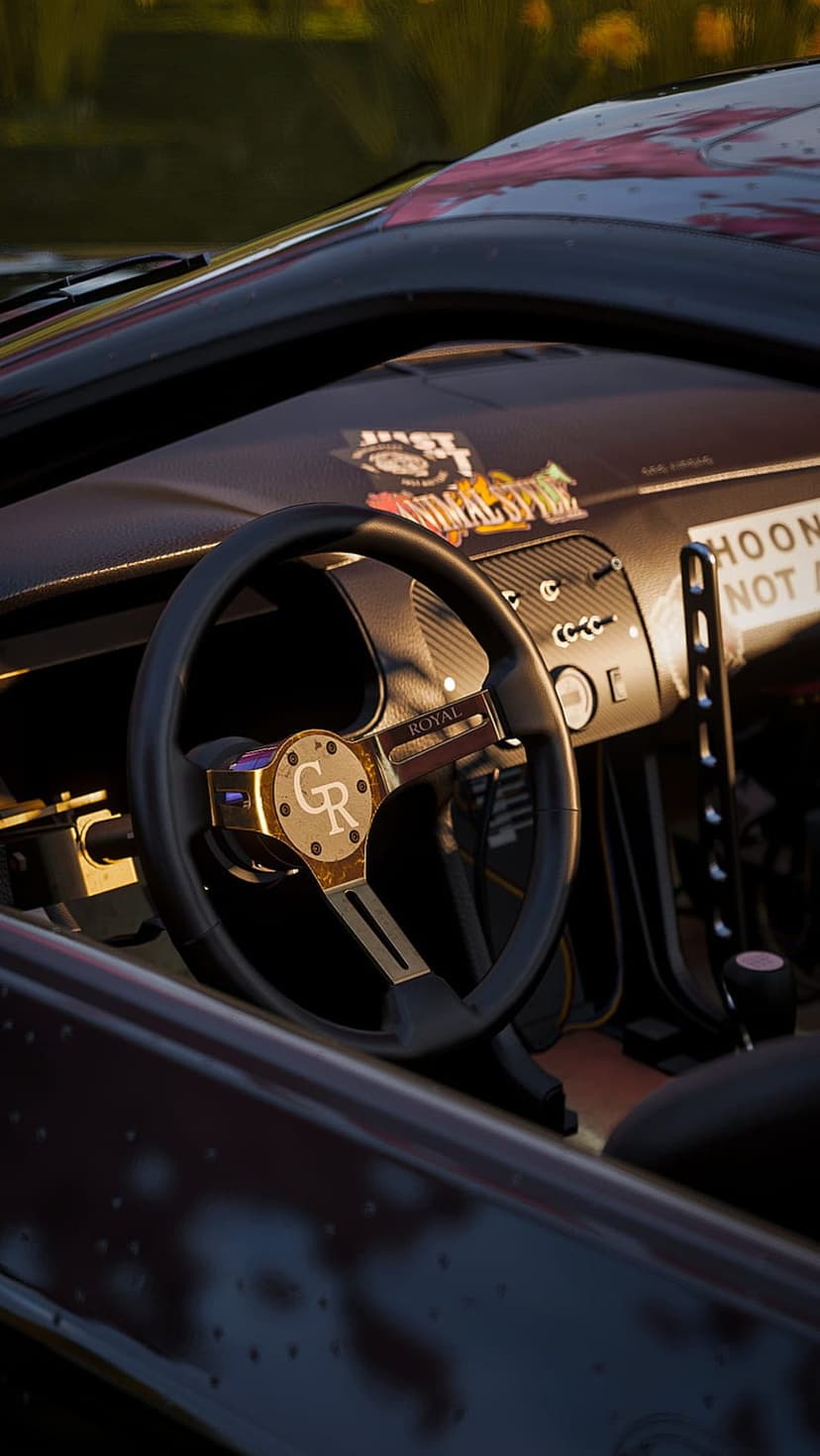 Gold-hubbed steering wheel with a CR logo and street racing stickers inside a modified drift car cabin.