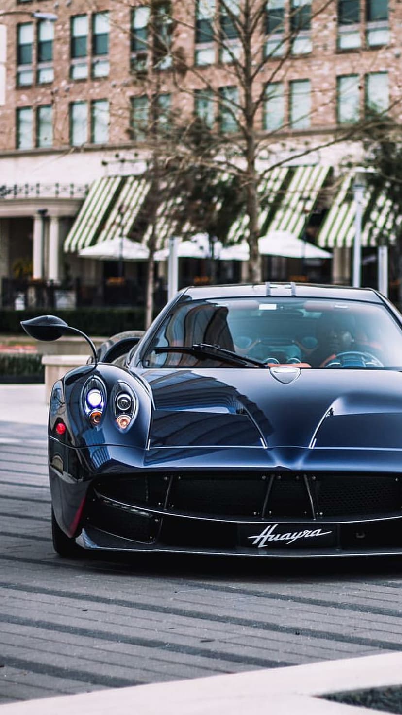 Pagani Huayra front grille and quad headlights in dark blue metallic paint with an urban street background.