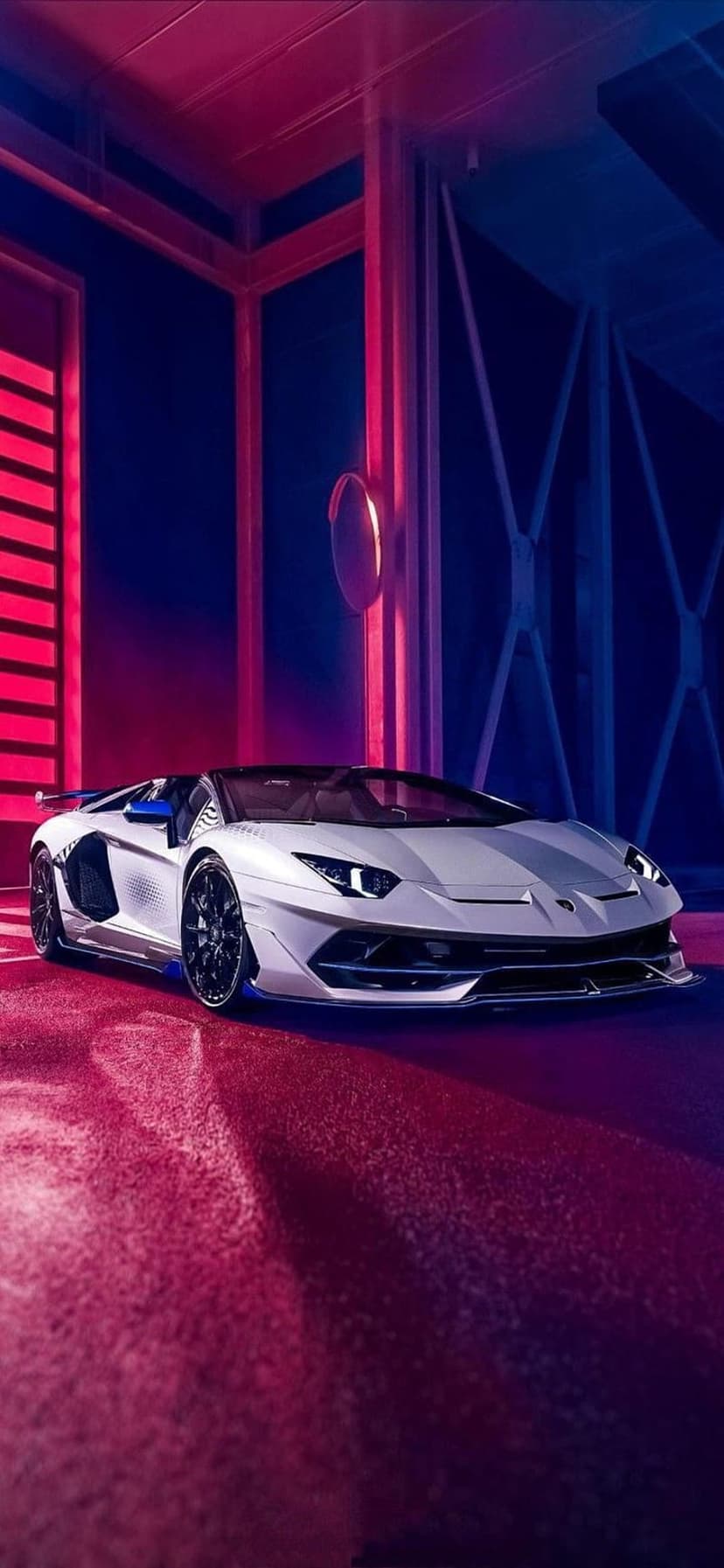 White Lamborghini Aventador in a dark garage with red and blue neon lights reflecting on a polished floor.