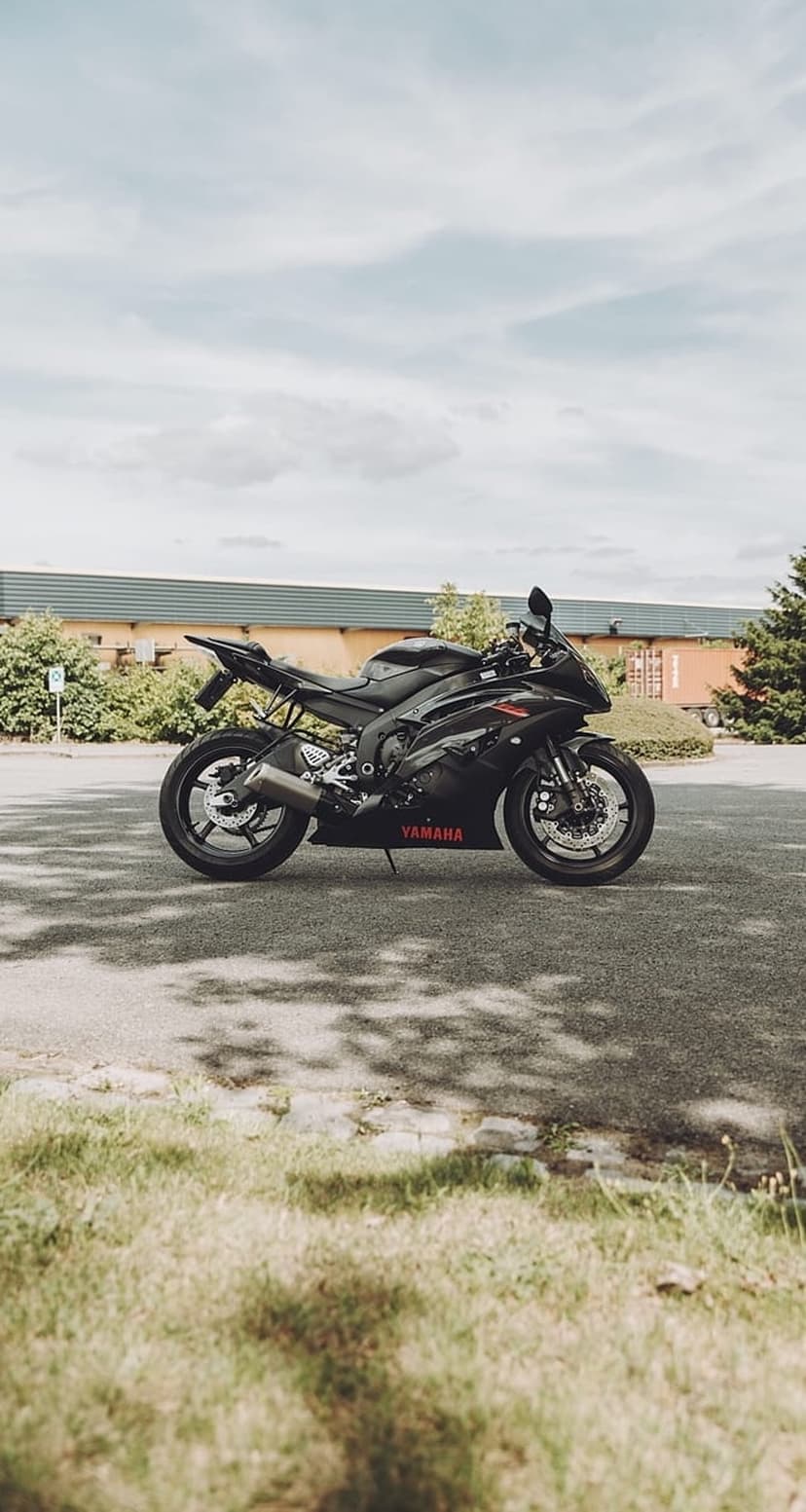Black Yamaha sportbike with red lettering parked on asphalt with green grass and tree shadows in view.