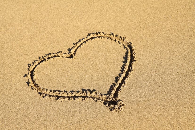 Heart shape hand-drawn in textured beach sand illuminated by warm golden sunlight during a coastal sunset.