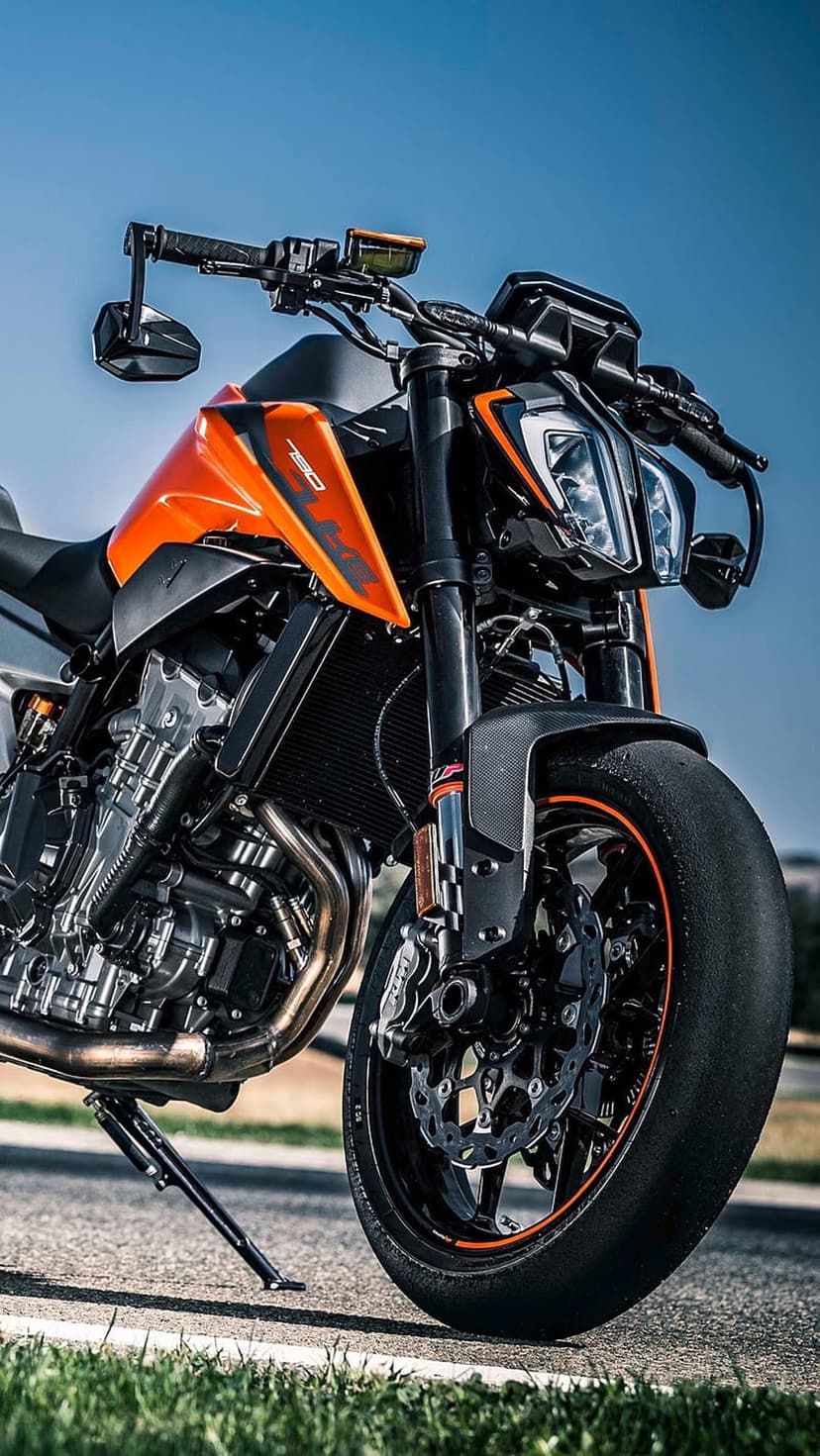 KTM 790 Duke motorcycle shows orange fairings and an exposed engine block under a clear blue sky atmosphere.