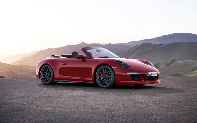 Red Porsche 911 GTS Cabriolet parked on a cracked asphalt road with a hazy mountainous landscape at sunset.