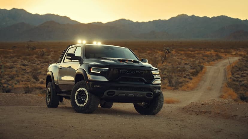 Dark RAM TRX off-road truck on a dirt path in a desert landscape with mountains under a golden sunset sky.