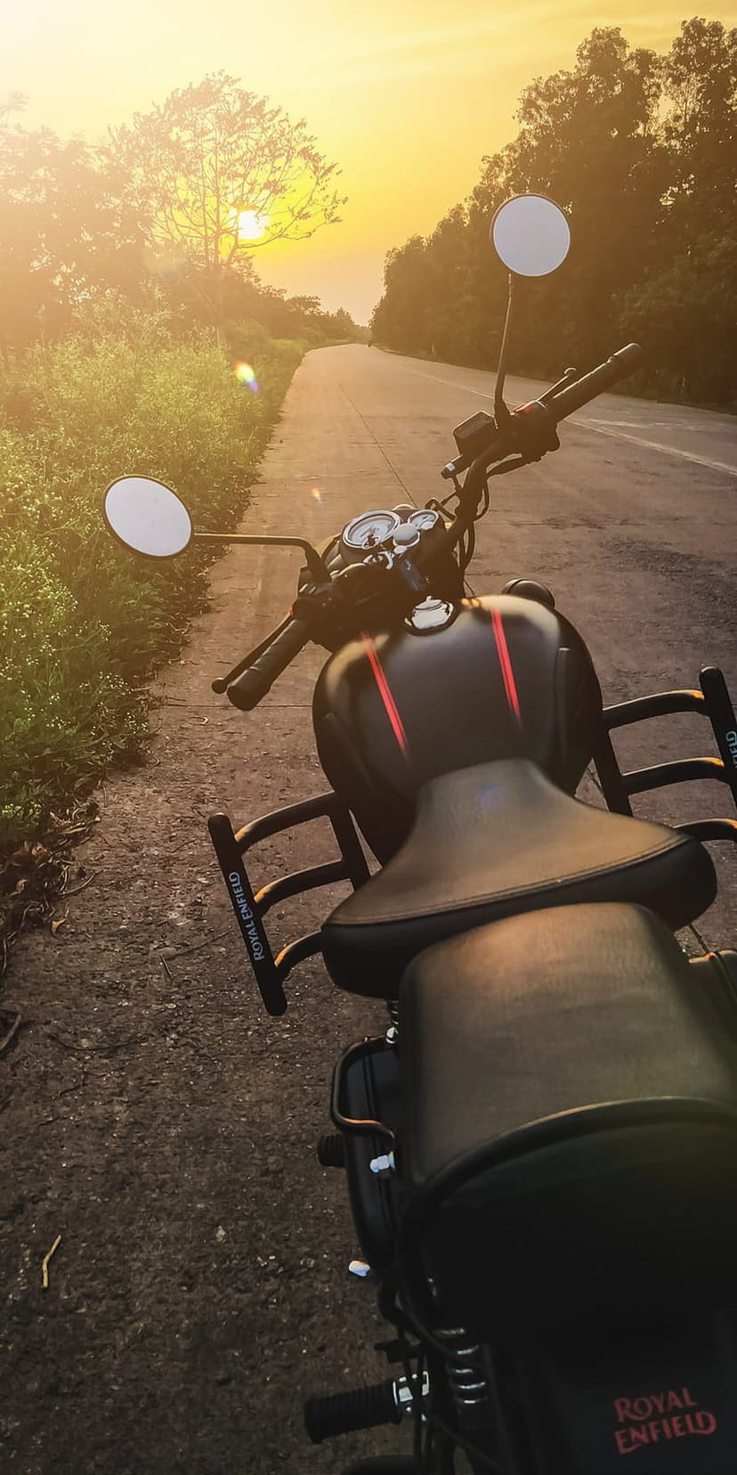 Royal Enfield motorcycle on an asphalt road at sunset with golden light hitting the handlebars and leather seat.