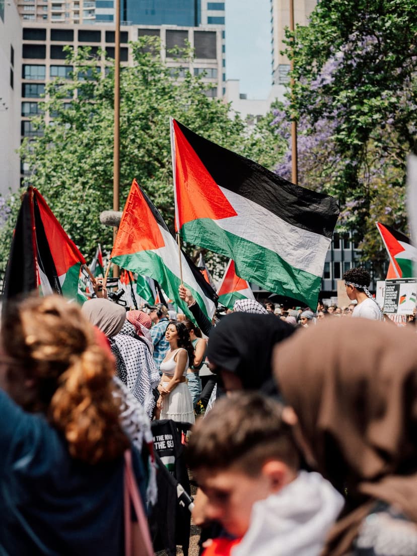 Palestinian flags wave prominently above a blurred crowd of protesters during an outdoor solidarity rally.