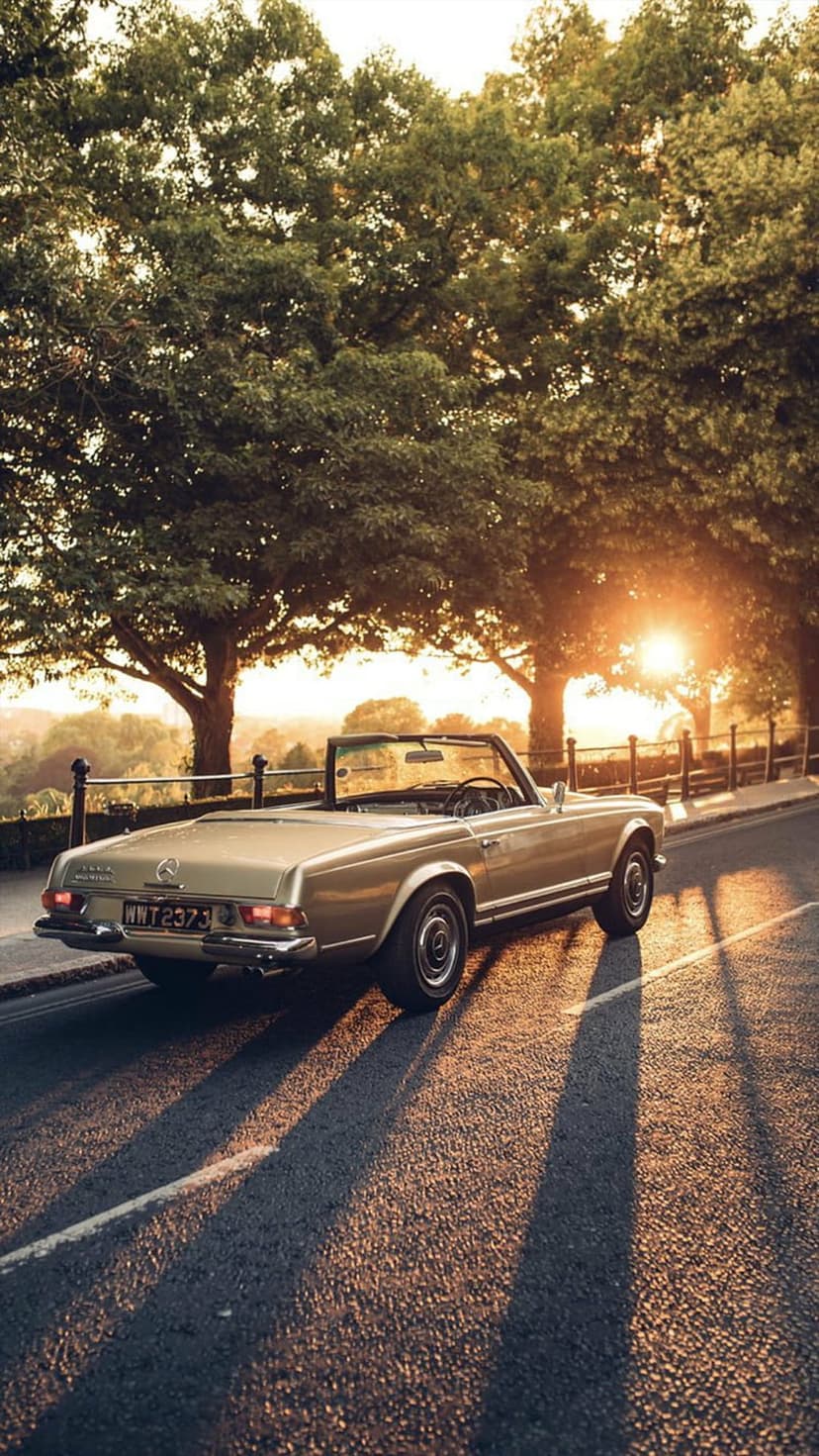 Mercedes-Benz convertible driving on a rural road at sunset with long shadows and warm golden hour light.