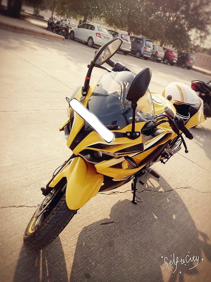 Yellow sport motorcycle with a helmet on the seat parked on sunny asphalt with trees and cars in the background.
