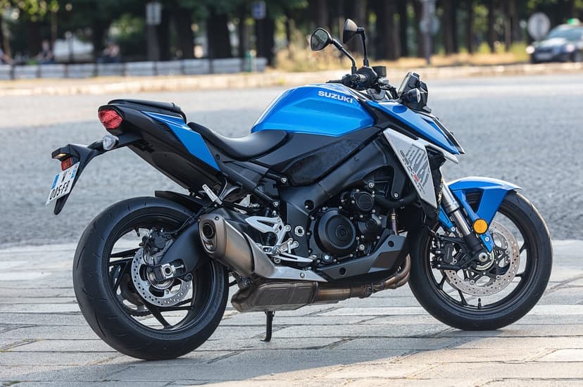 Side view of a blue and black Suzuki GSX-S950 motorcycle parked on a paved city square with a blurred background.