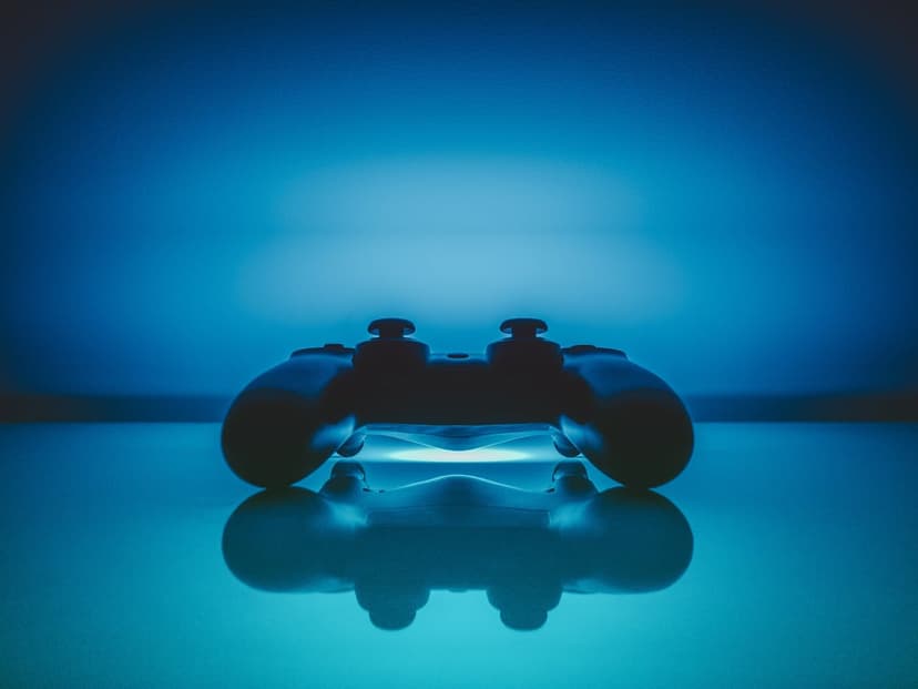Black gaming controller with glowing blue internal lights sits on a glossy dark surface with a clear reflection.