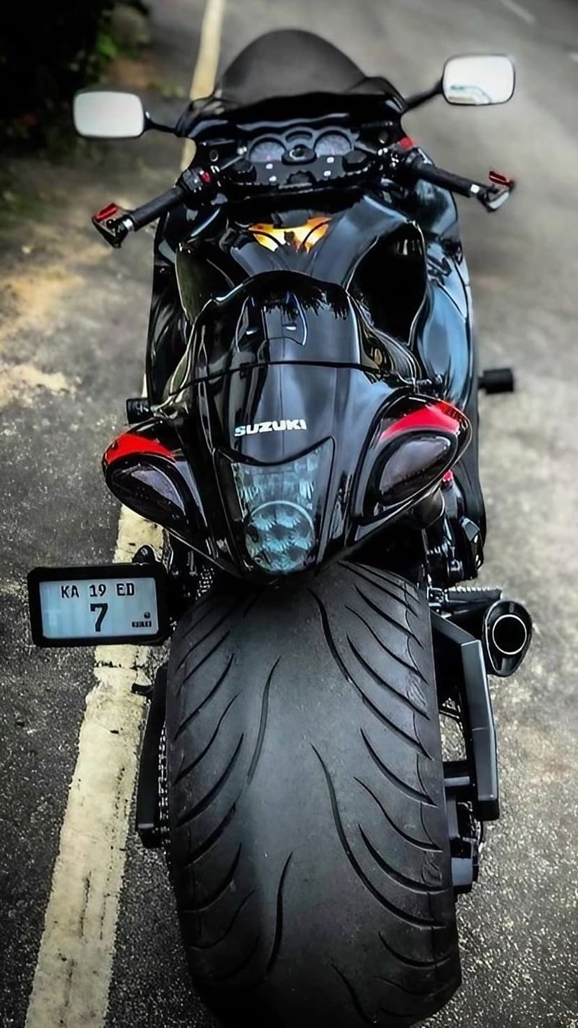 Suzuki Hayabusa motorcycle rear view showing the wide tire, twin exhaust, and red tail light on a black body.