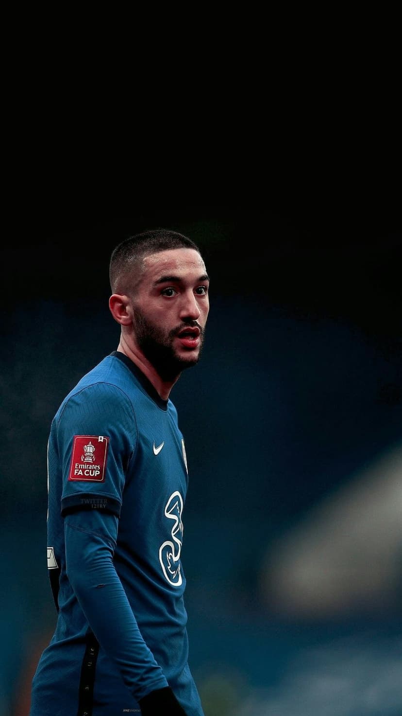 Hakim Ziyech in a blue Chelsea jersey with a tournament badge on the sleeve against a dark stadium backdrop.