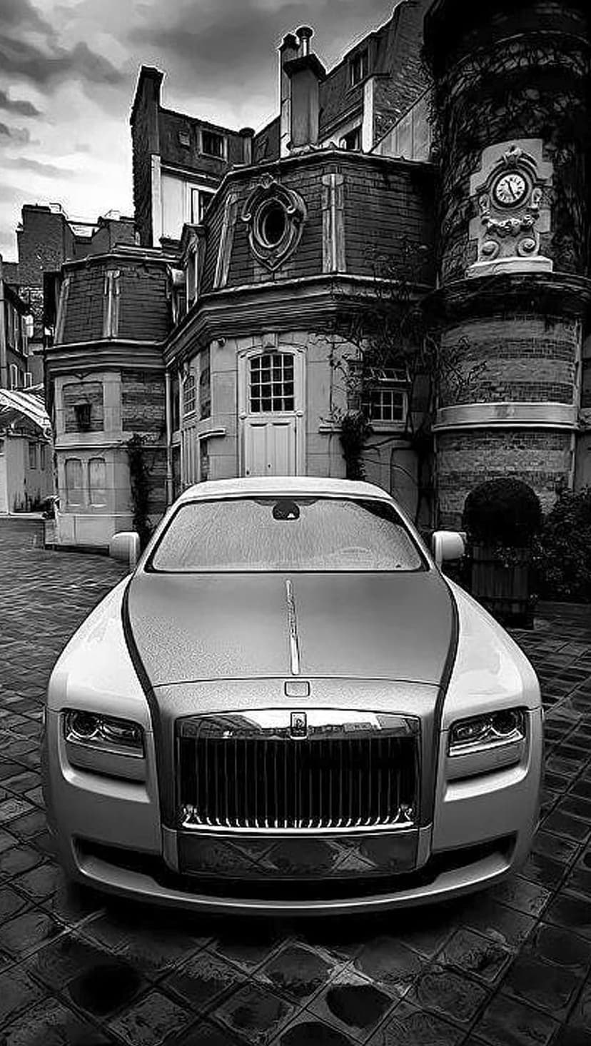 Rolls-Royce Ghost luxury car parked on wet cobblestones in front of a historic European stone building at dusk.